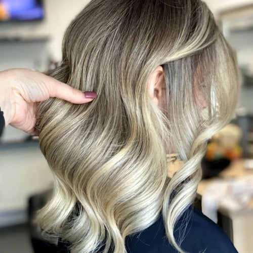 A hand showcasing wavy blonde hair with soft curls in a salon setting